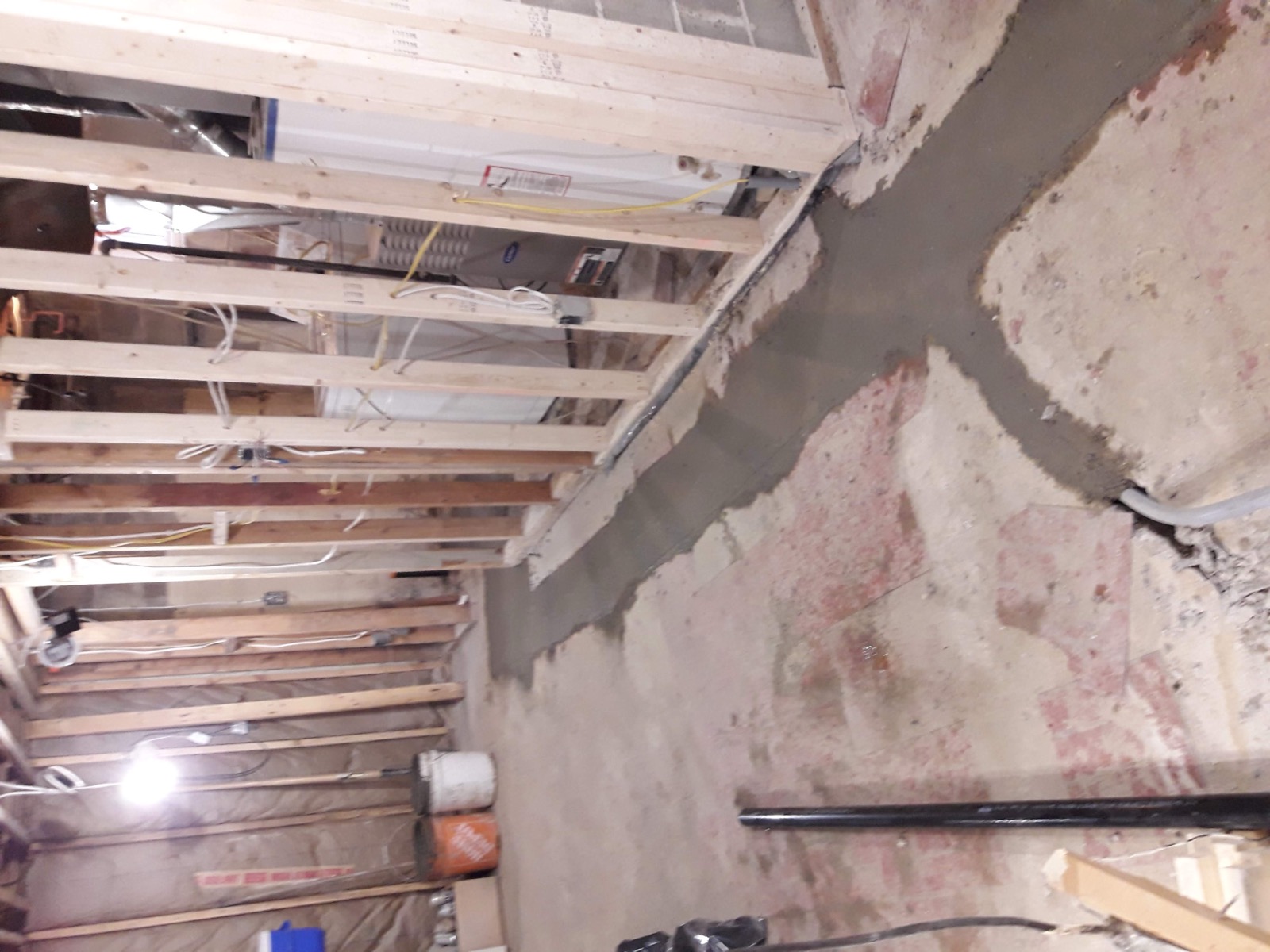 Basement before renovation — bare concrete floor, exposed ceiling joists, unfinished walls