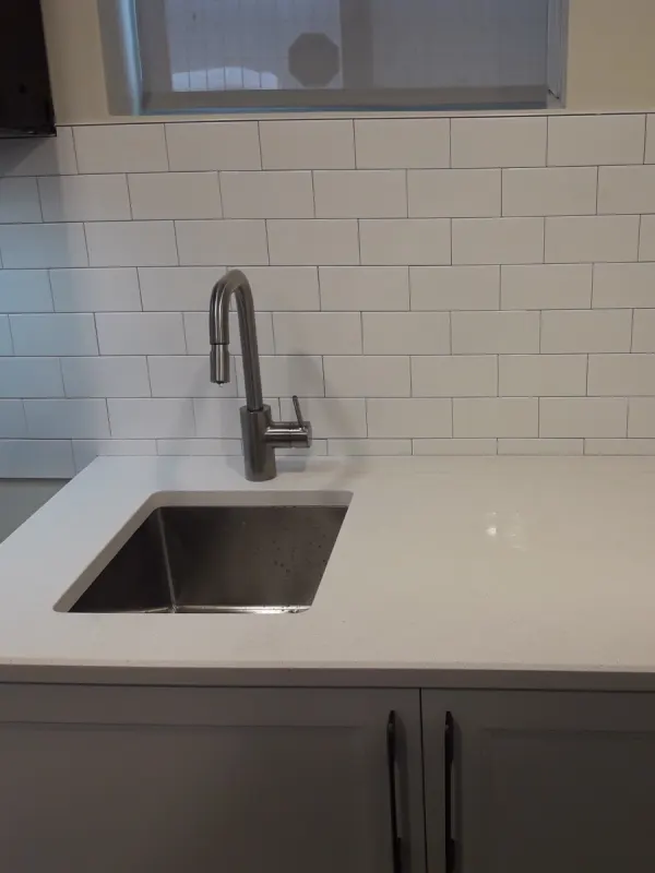 Undermount stainless sink in a white quartz counter with a gooseneck faucet and a white subway-tile backsplash